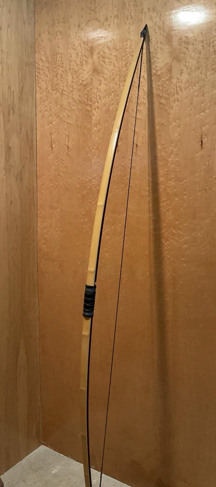 The 115-pound bamboo-backed ipe warbow, strung and standing full length against the maple wall