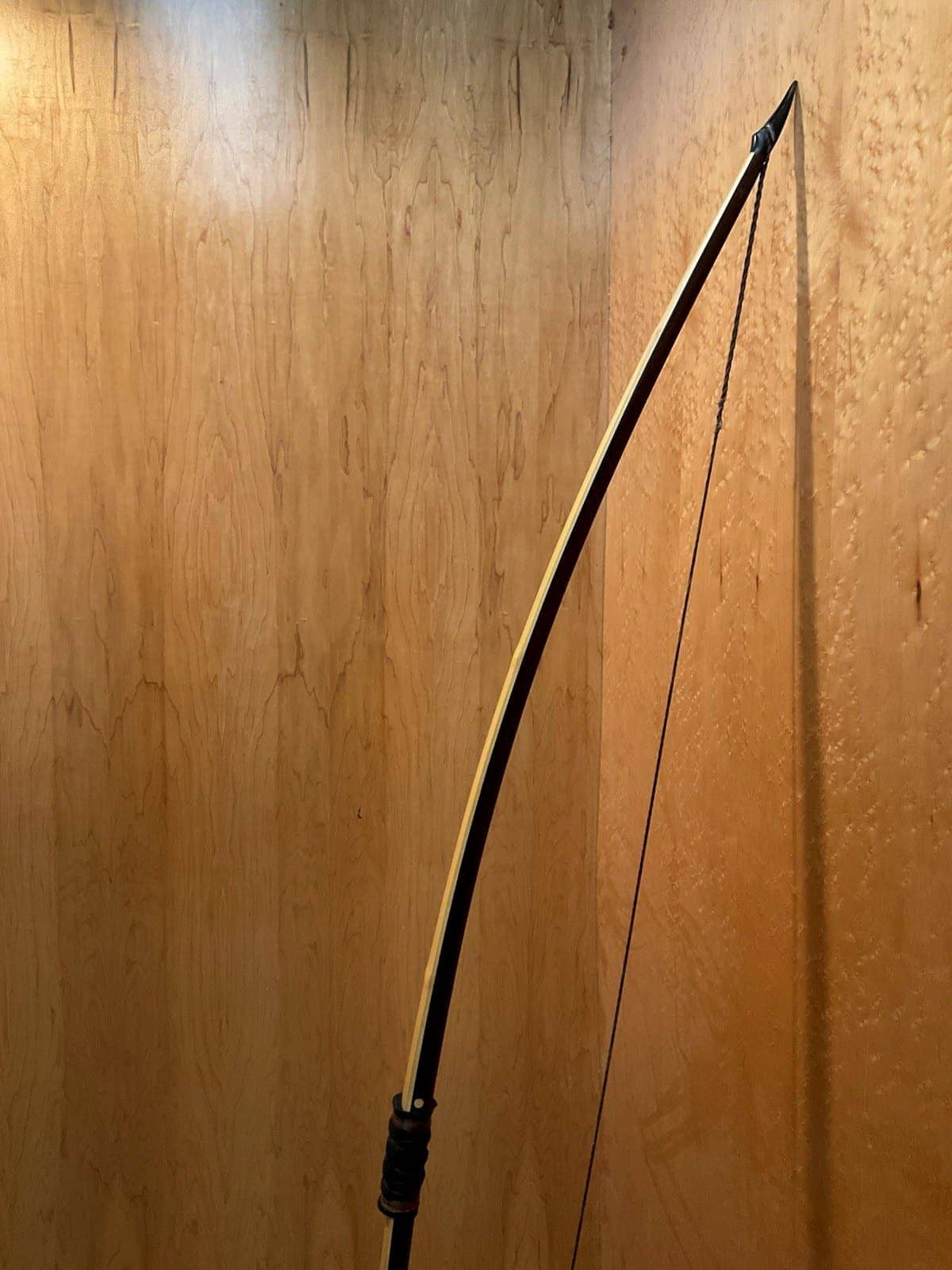 The curve of the 150-pound bamboo-backed ipe warbow, standing against the maple wall