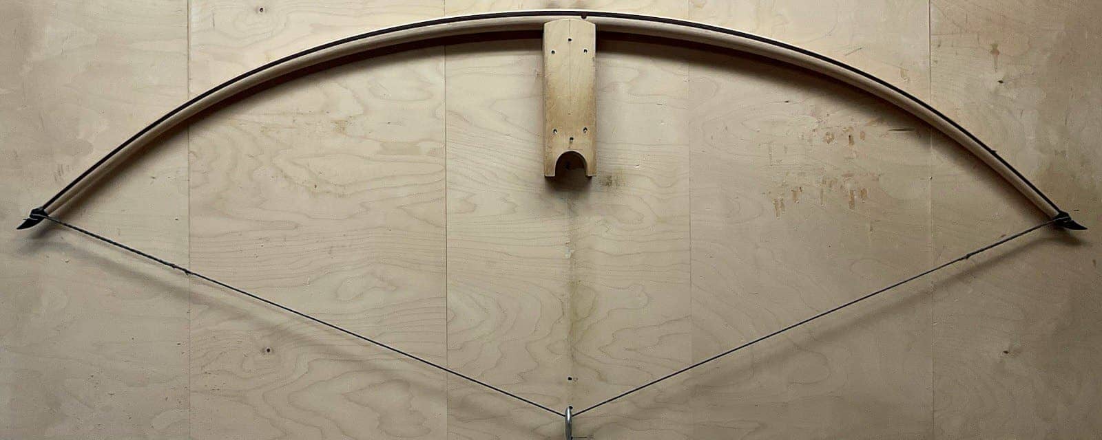 The 180-pound bamboo-backed tri-lam warbow, braced and hung on a wall peg