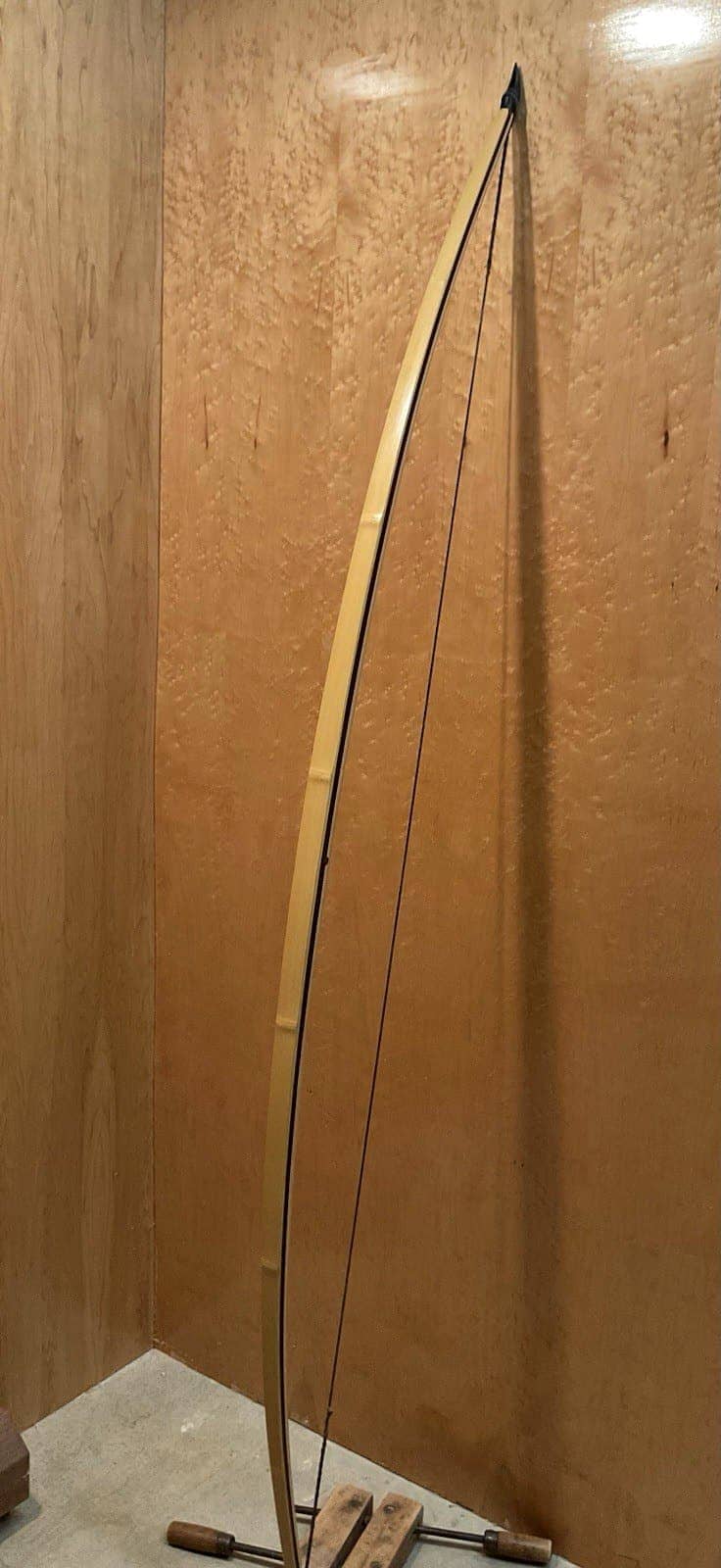 The 180-pound bamboo-backed tri-lam warbow, strung and standing full length against the maple wall