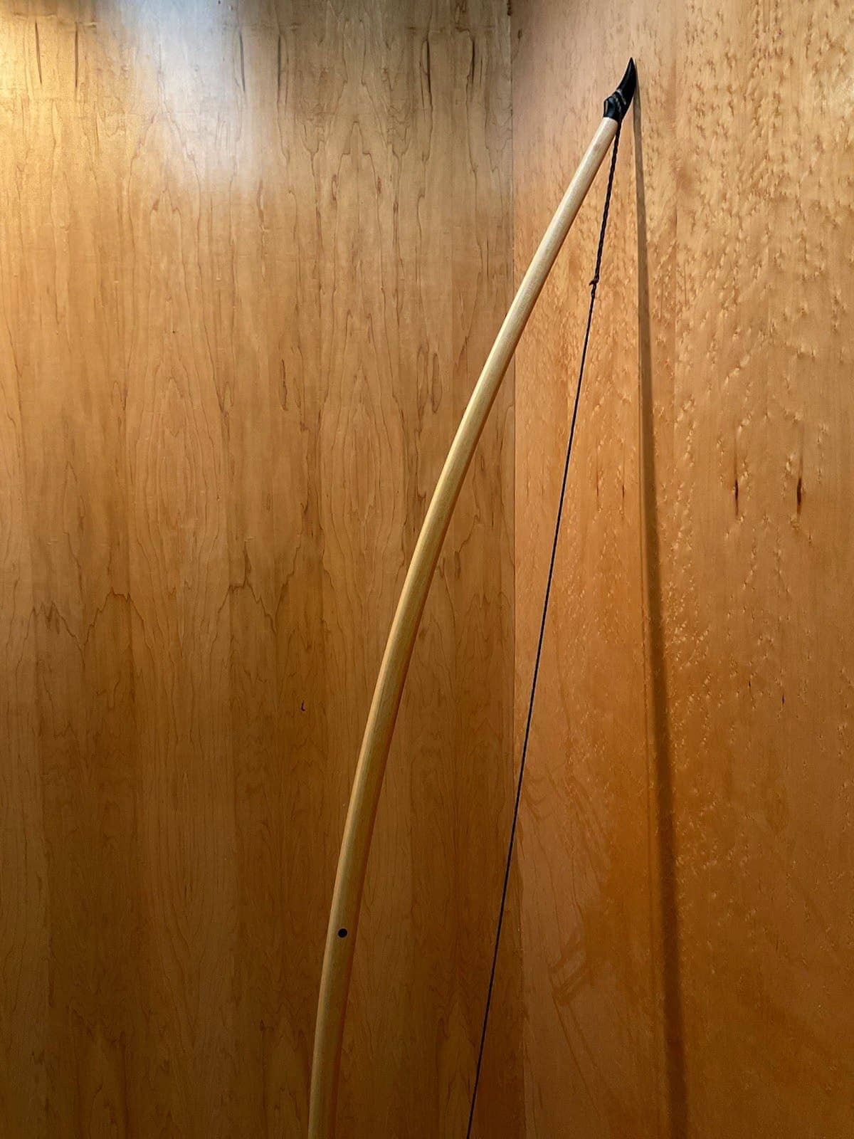 The curve of the 190-pound white hickory selfbow warbow, standing against the maple wall