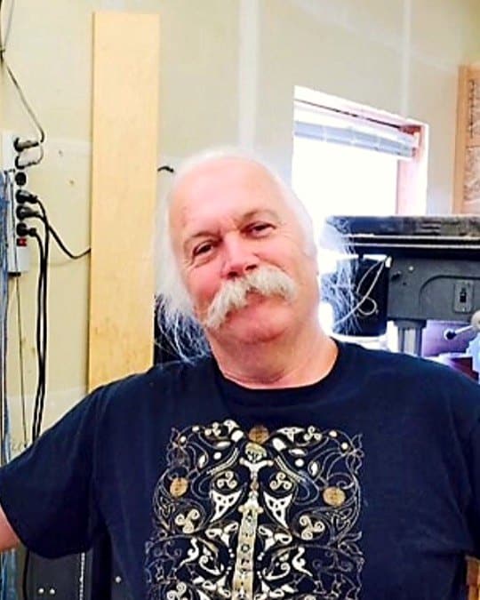 Doug Parry, white-haired with a long white moustache, smiling in his workshop